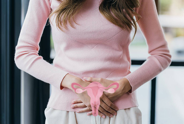 ピンクの服を着た女性が下腹部に手を当て、その上に子宮のイメージ画像がある